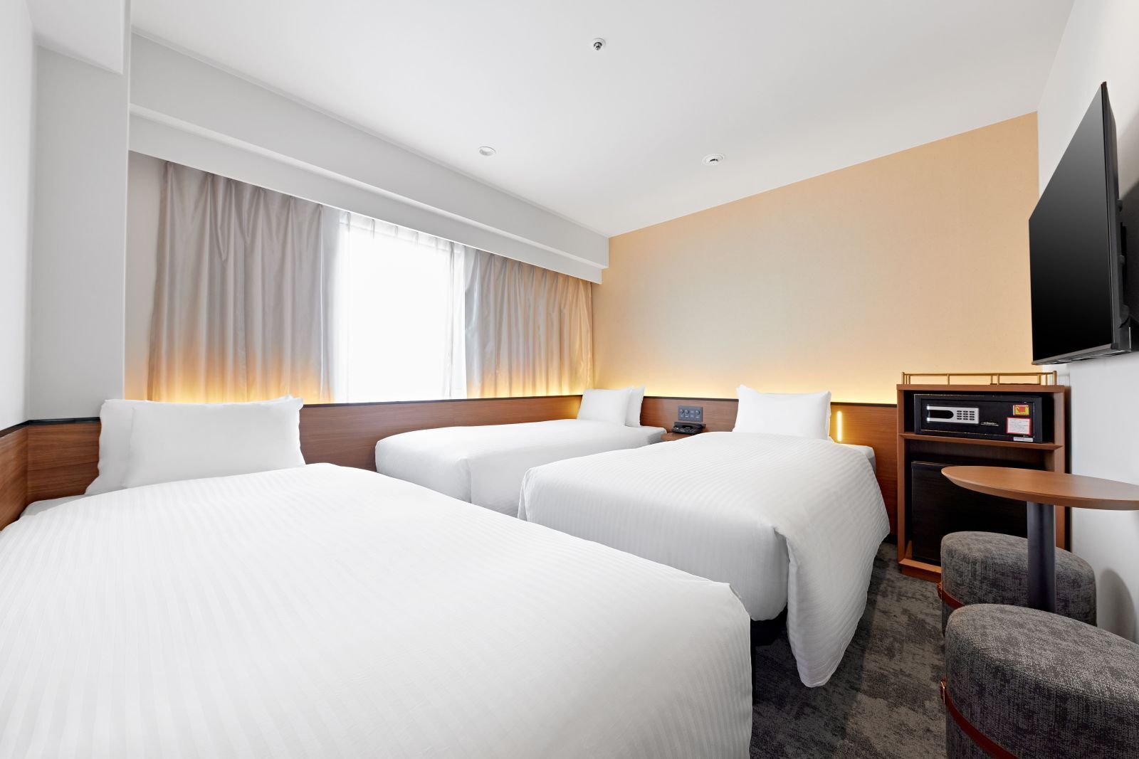 A hotel room with two beds, a desk, a chair, a flat-screen TV, and a window with curtains.