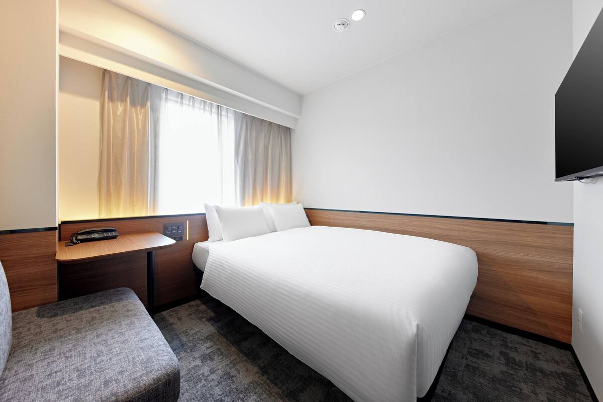 Een hotelkamer met een bed, een bureau, een stoel, een televisie en een raam met gordijnen.