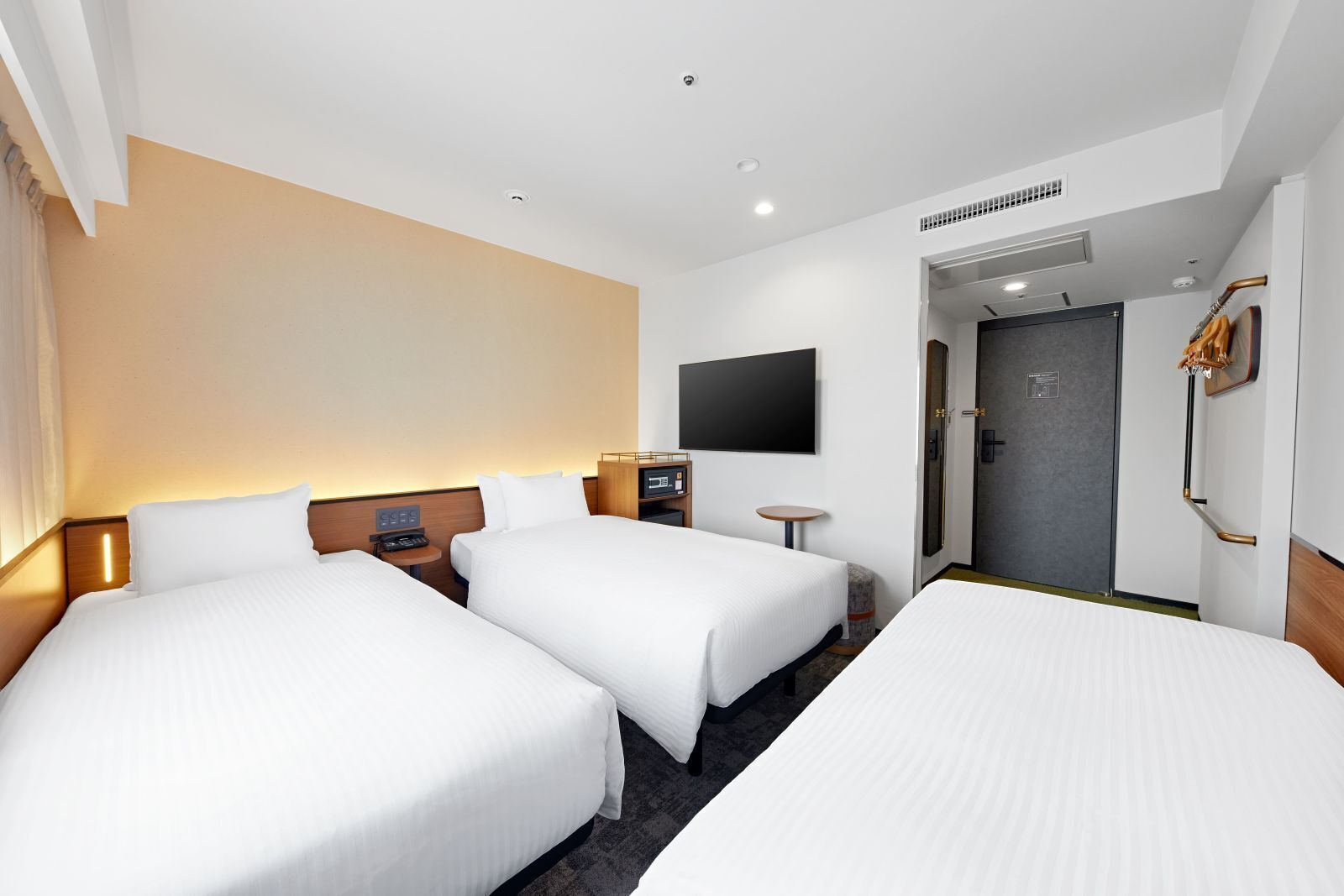 A hotel room with three beds, a flat-screen TV, a desk, and a shower area.