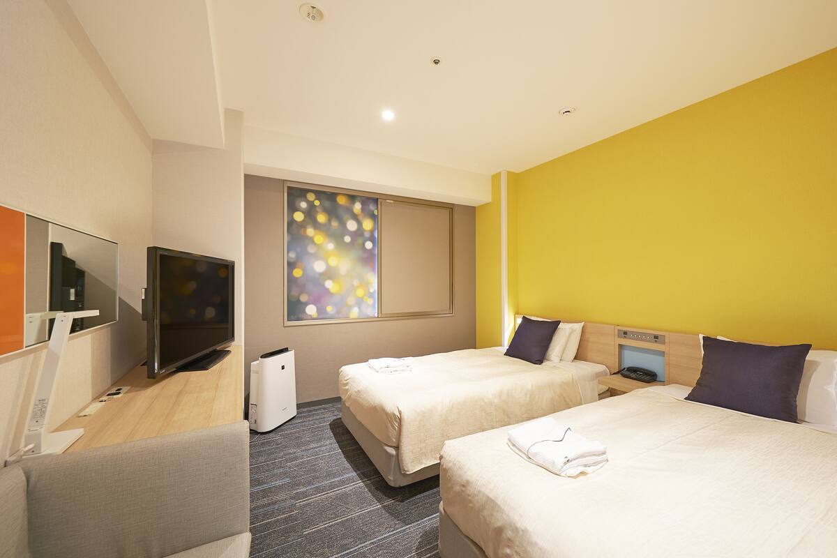 Een hotelkamer met twee bedden, een televisie, een bureau en een raam met uitzicht op de stad.