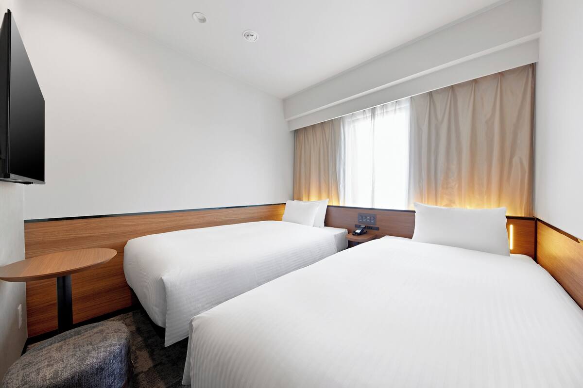 Een hotelkamer met twee bedden, een flatscreen televisie, een nachtkastje en een raam met gordijnen.