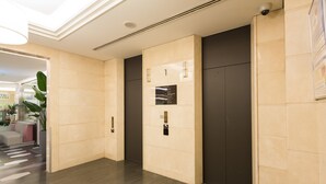 A modern elevator area with a marble floor, a wall-mounted elevator control panel, and a security camera. - Sotetsu Grand Fresa Osaka - Namba (Osaka)