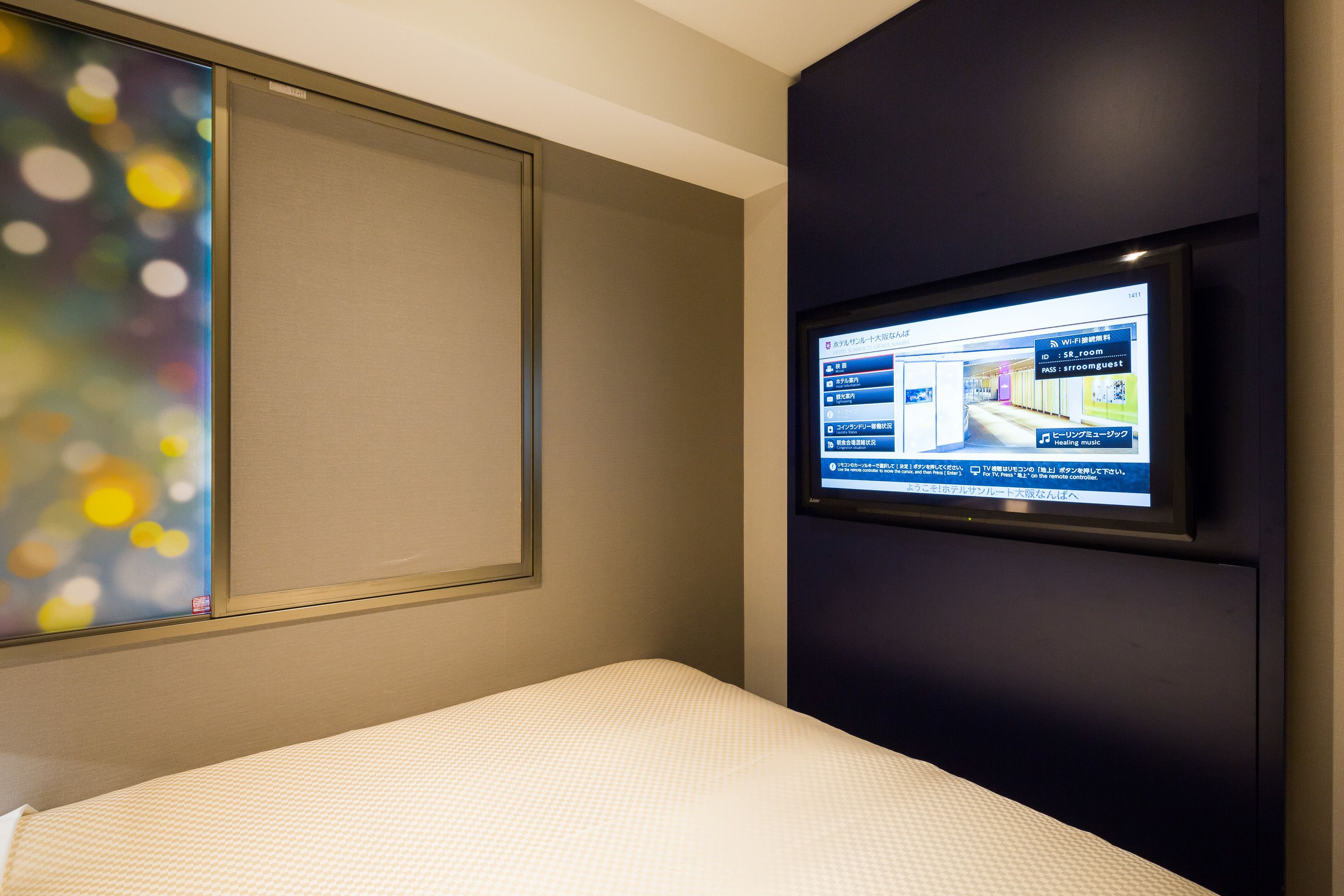 Habitación de hotel con cama, televisor montado en la pared y ventana con vistas a la ciudad.