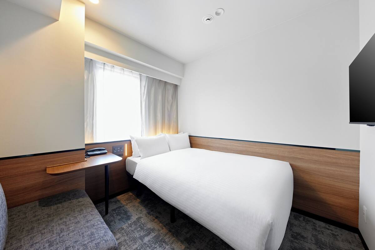Hotelkamer met een bed, bureau, stoel, televisie en raam met gordijnen.