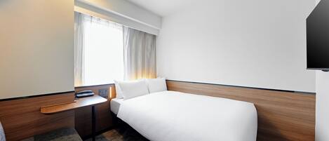 A hotel room with a bed, a desk, a chair, a TV, and a window with curtains.