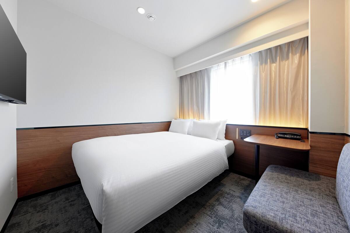 Hotelkamer met een groot bed, een tafeltje, een stoel, een televisie en een raam met gordijnen.