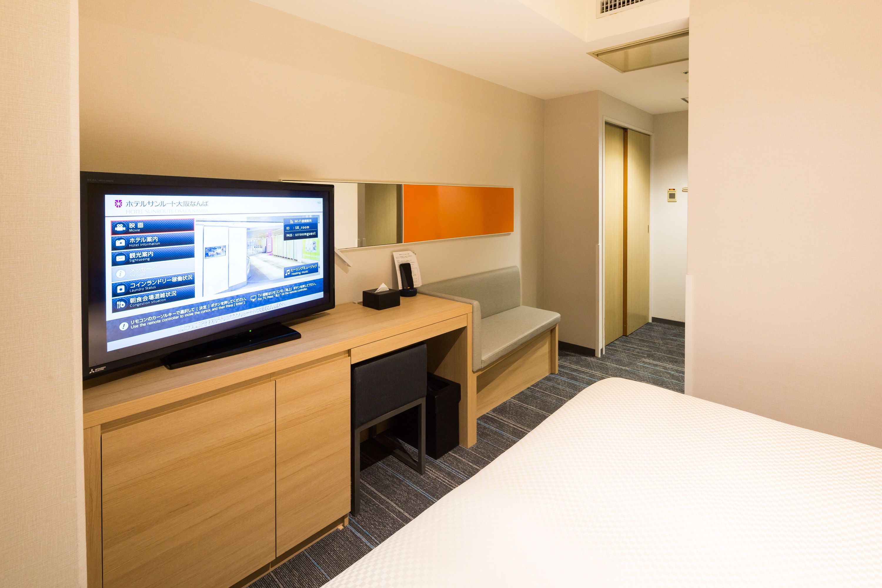 A hotel room with a bed, a desk with a computer monitor, a chair, and a small table.