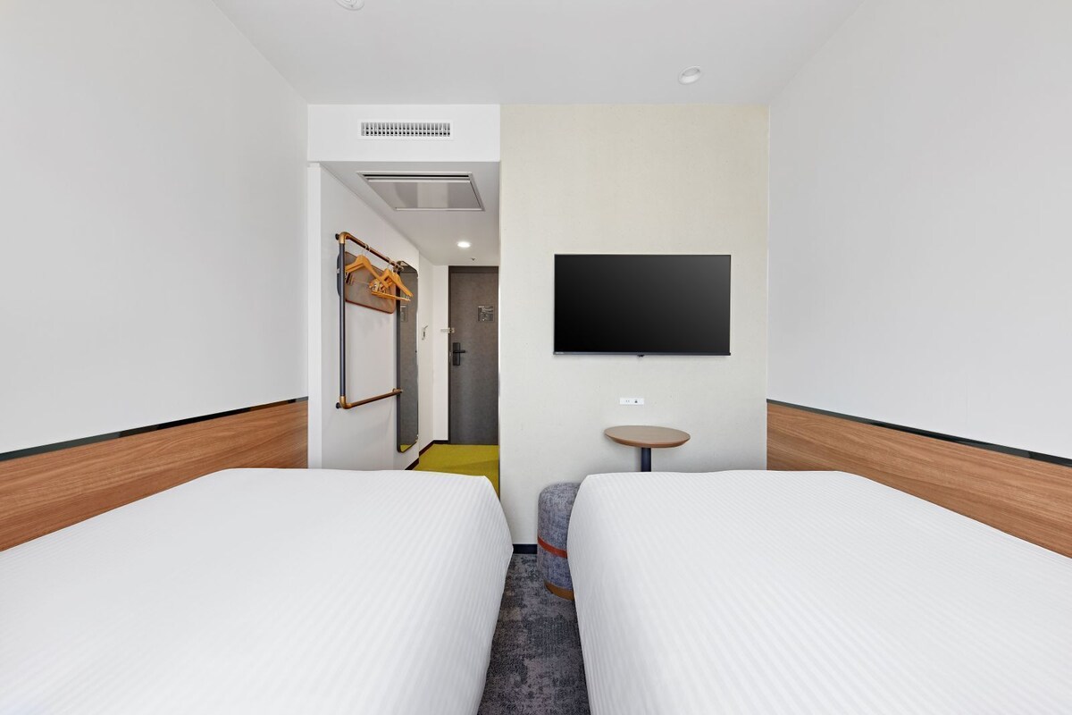 Een hotelkamer met twee bedden, een aan de muur bevestigde televisie, een tafeltje en een kapstok.