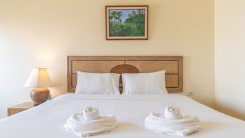 Habitación de hotel con una cama bien hecha, dos almohadas, cabecera de madera, un cuadro en la pared y una lámpara en la mesita de noche.