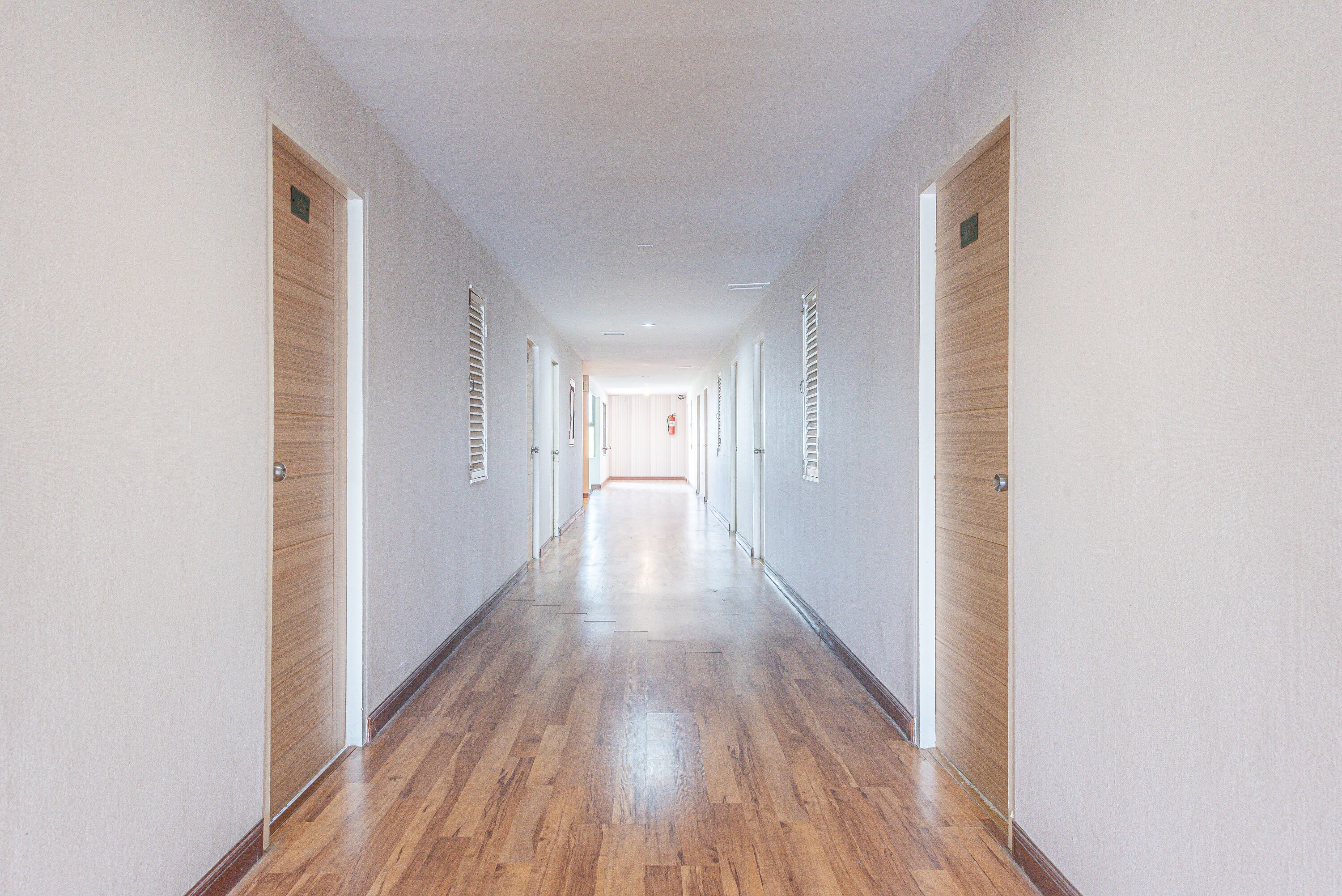 A long, narrow hallway with wooden flooring and white walls, leading to a door at the end.