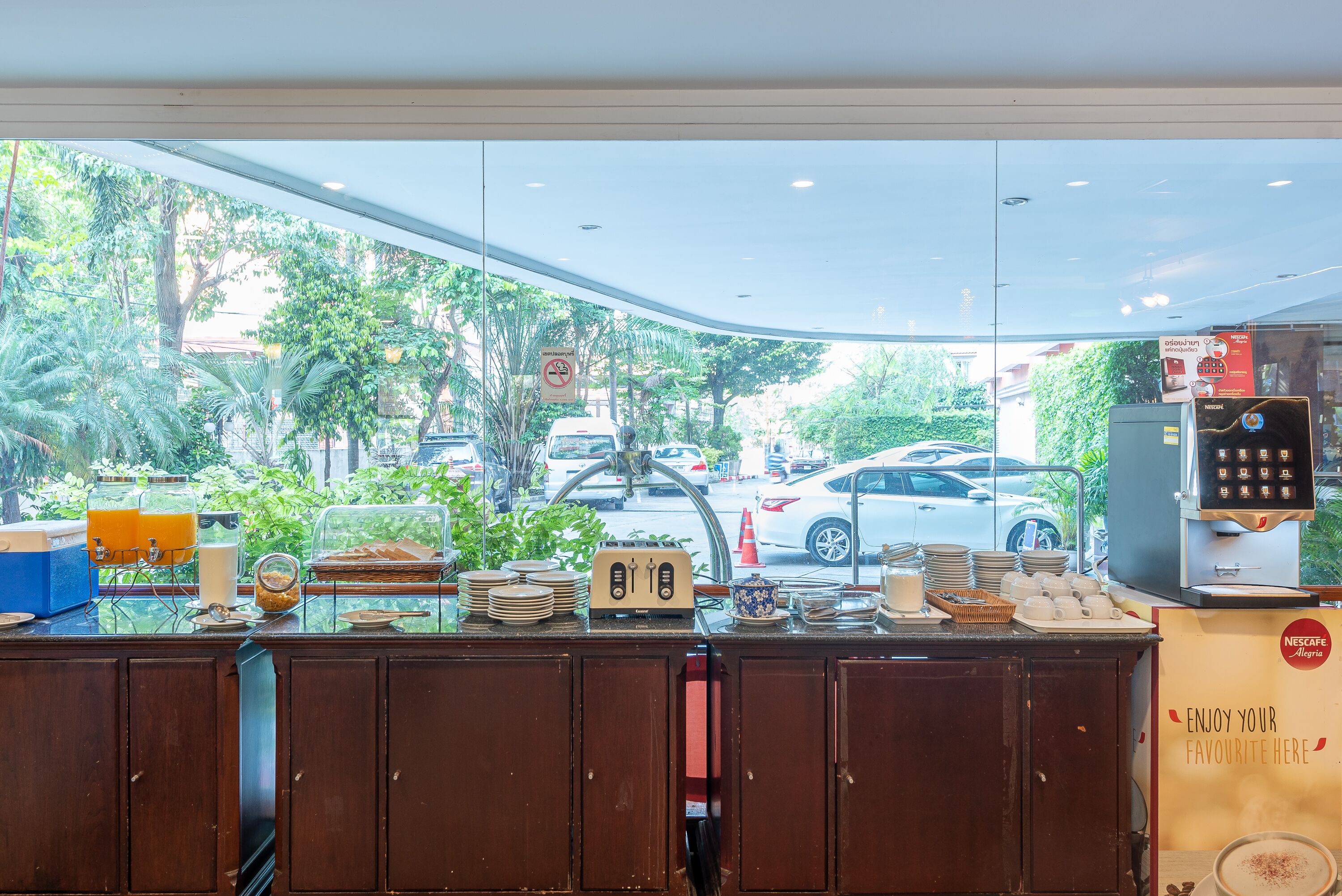 A cafe counter with a variety of food items and a coffee machine, with a view of the street outside.
