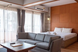 A hotel room with a sofa, a bed, a table, and a large window with curtains. - Nonthaburi Palace Hotel (Nonthaburi)