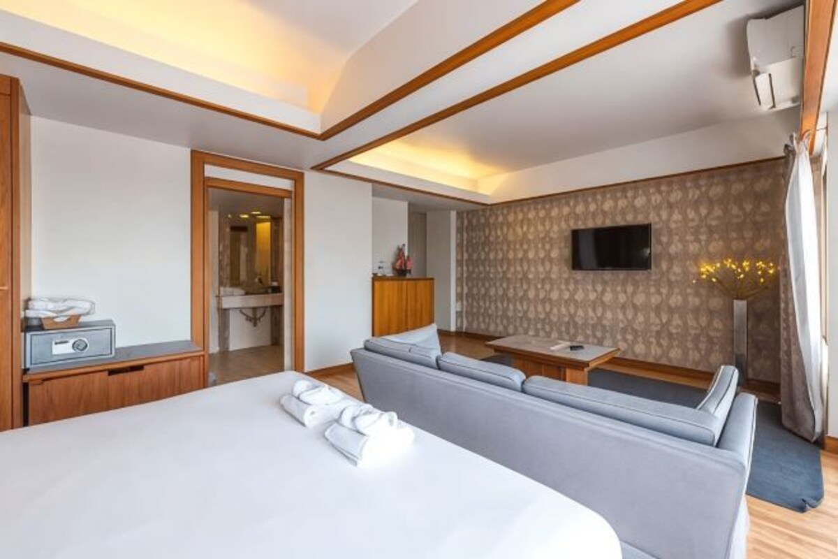 A hotel room with a large bed, a sofa, a TV, and a desk.