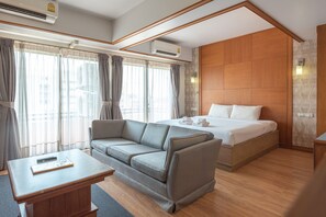 A modern hotel room with a wooden bed, grey sofa, and a small table. - Nonthaburi Palace Hotel (Nonthaburi)
