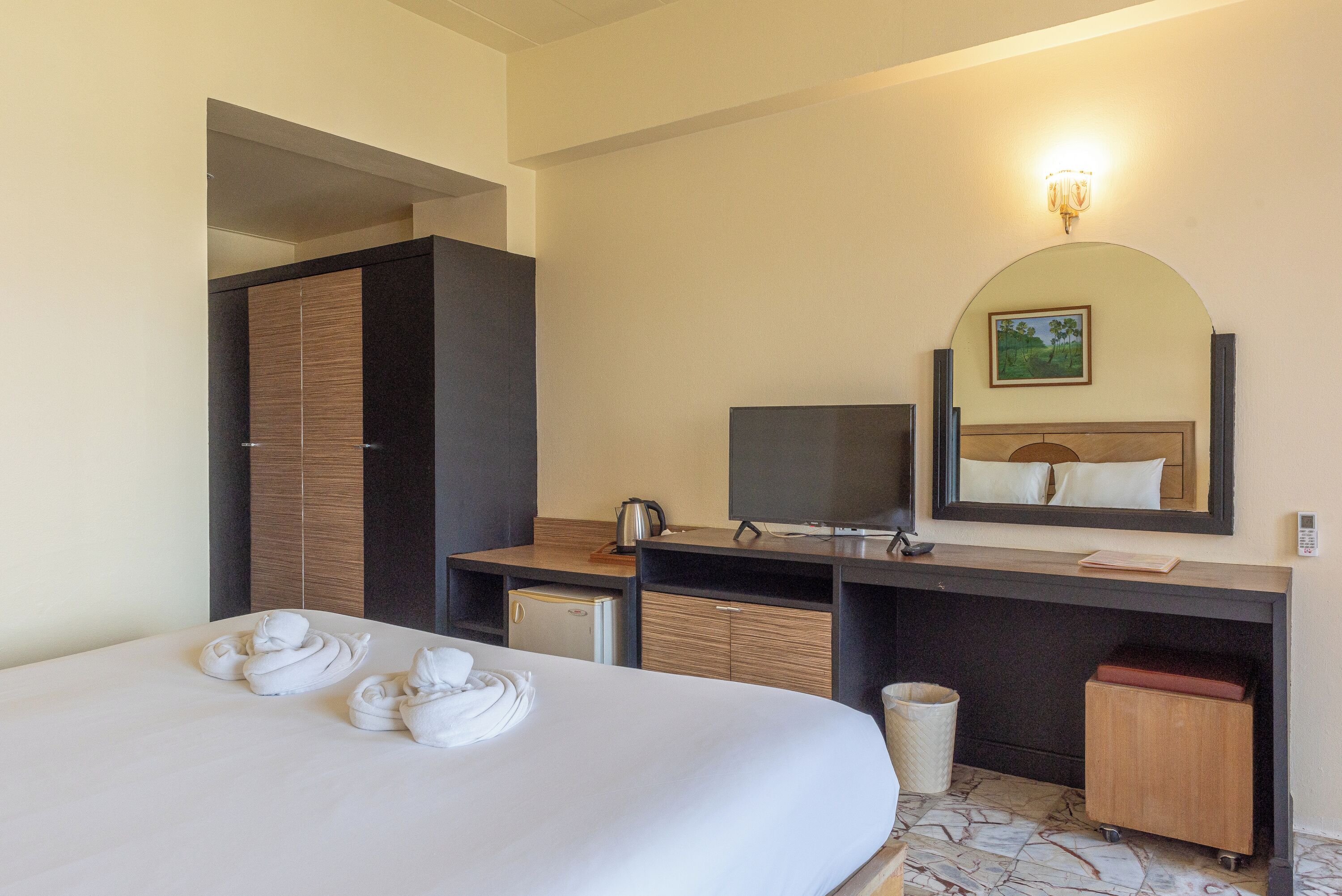 A hotel room with a bed, a desk, a television, a mirror, and a small kitchenette.