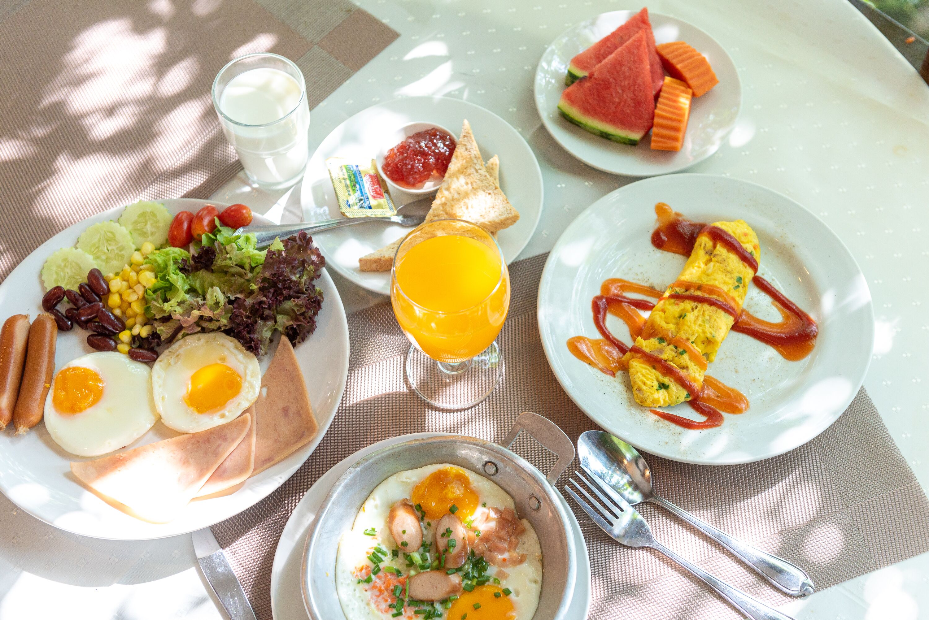 Uma mesa de café da manhã com pratos de ovos, torradas e frutas, um copo de suco de laranja e uma tigela de sopa.