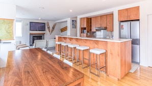 A modern kitchen with wooden cabinets, a stainless steel refrigerator, and a bar area with stools. - Wajima Niseko (Kutchan)