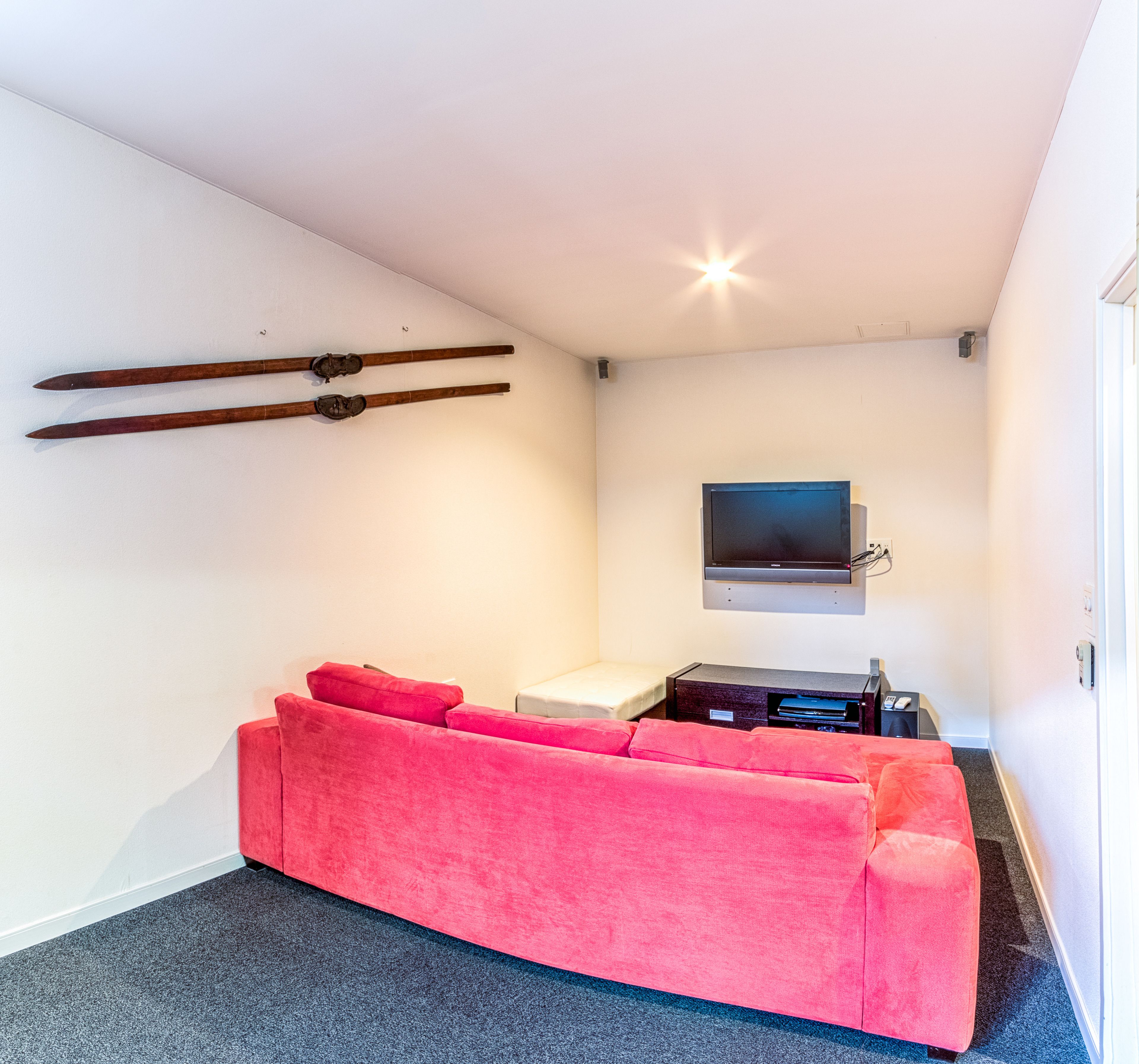 A modern room with a pink sofa, a flat-screen TV mounted on the wall, and skis leaning against the wall.