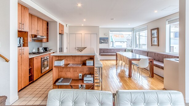 A modern kitchen with wooden cabinets, a dining area with a bench, and a view of the outside. - Wajima Niseko (Kutchan)