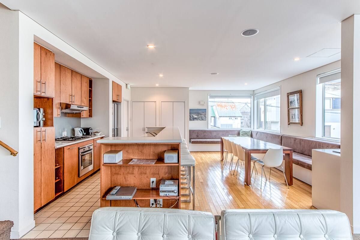 A modern kitchen with wooden cabinets, a dining area with a bench, and a view of the outside.
