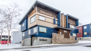 A modern multi-story residential building with a mix of wood and metal exterior, a stone base, and large windows. - Wajima Niseko (Kutchan)