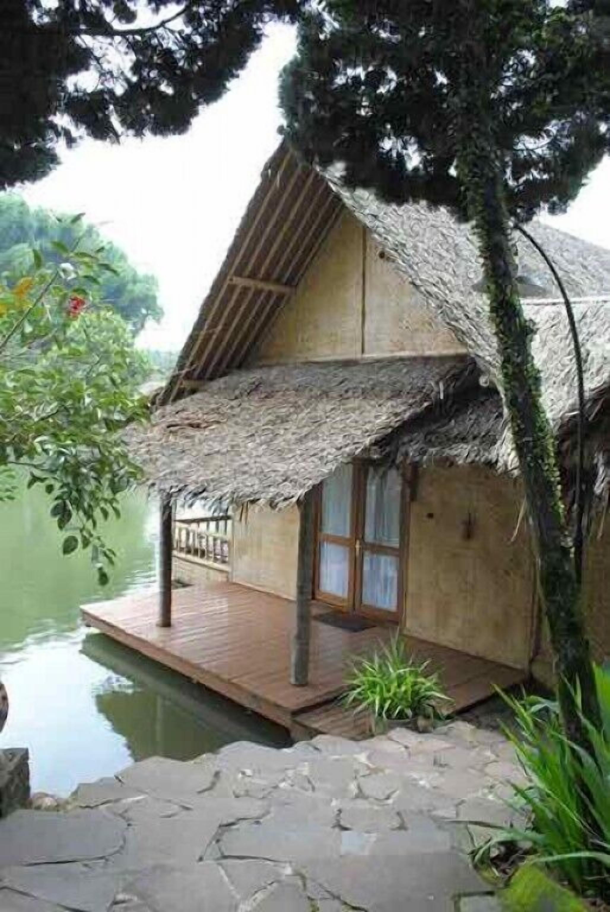 Une maison à toit de chaume avec une terrasse en bois qui s’étend au-dessus de l’eau.