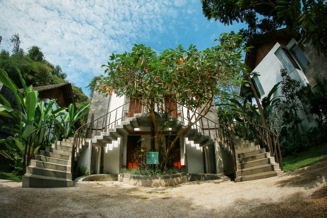 A staircase leading to a building with a modern design, surrounded by greenery and a clear sky.