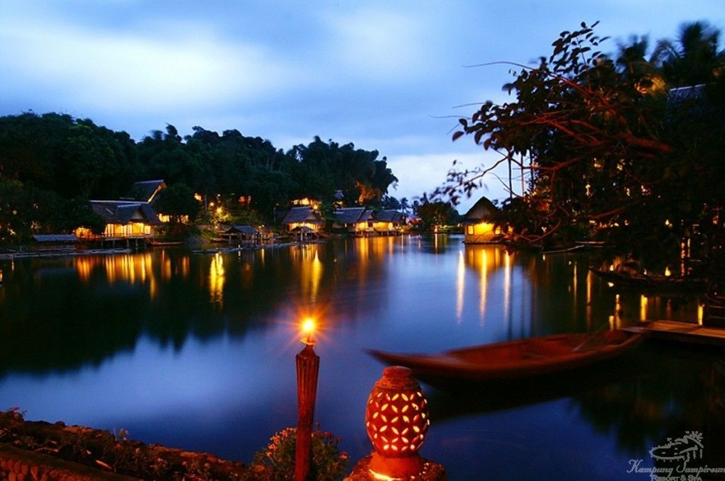 Une vue paisible sur un lac au crépuscule, avec des bâtiments illuminés qui se reflètent dans l'eau, un bateau et une lanterne traditionnelle.