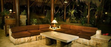 A cozy outdoor seating area with a stone bench and a sofa, a table, and a lamp.
