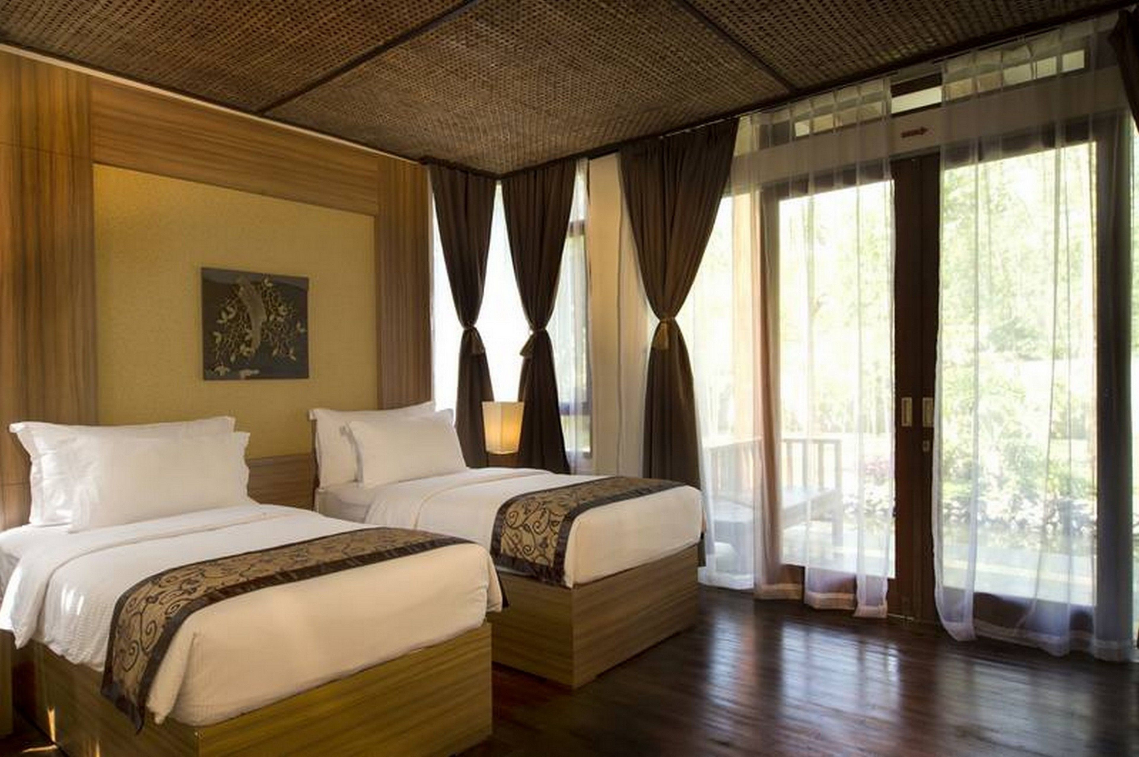 Habitación de hotel con dos camas, un ventanal con cortinas, un ventilador de techo y un cuadro en la pared.