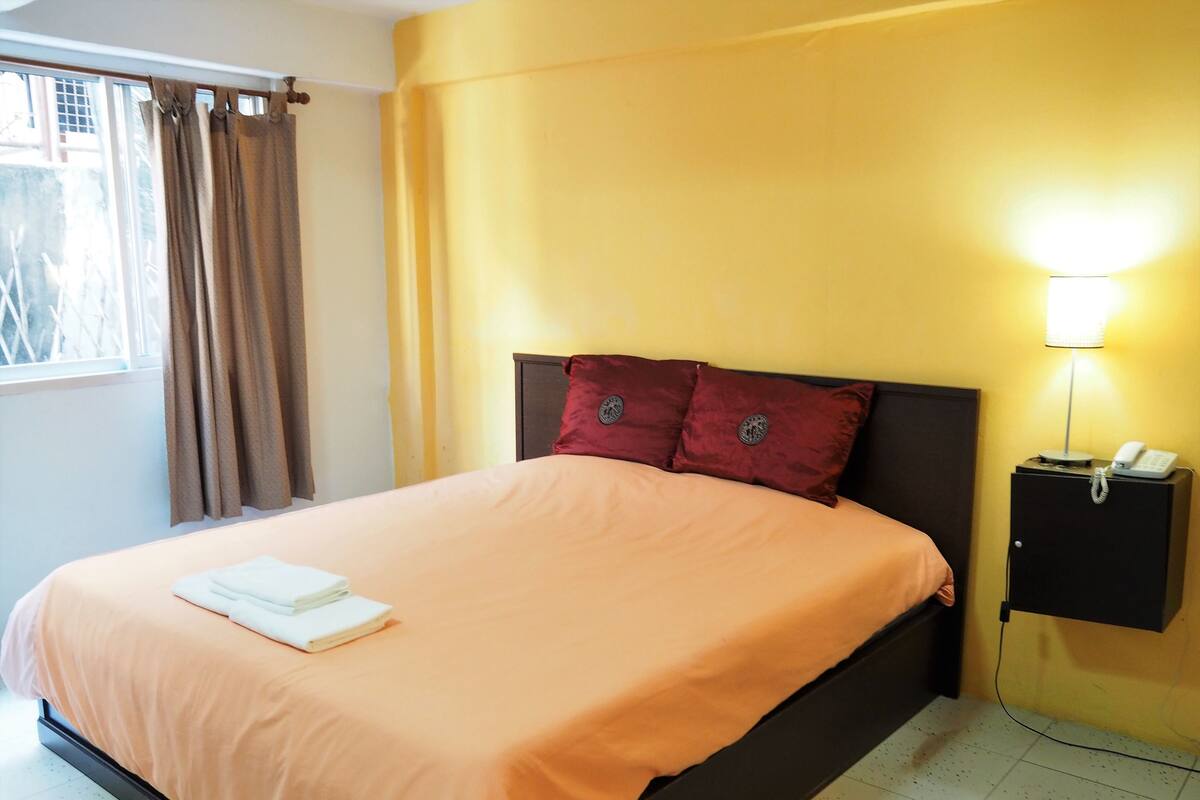 A hotel room with a bed, a nightstand with a phone, and a window with curtains.