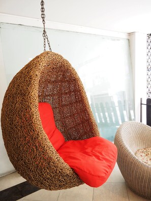 Una poltrona amaca con seduta intrecciata e cuscino rosso, sospesa al soffitto.