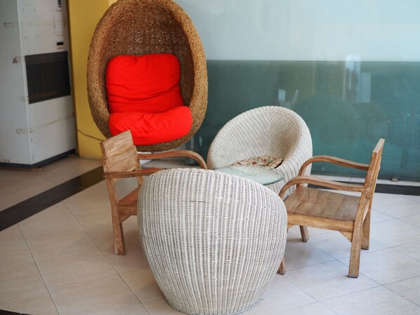 Wicker chairs with cushions and a woven ottoman in a room with a tiled floor and a glass partition.