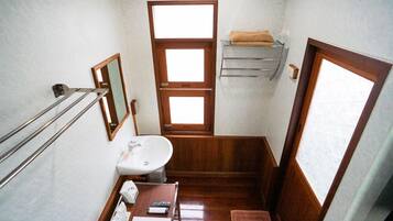 A compact bathroom with a sink, mirror, towel rack, and a small table with toiletries.