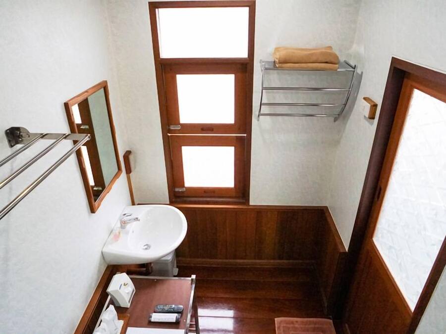 A compact bathroom with a sink, mirror, towel rack, and a small table with toiletries.