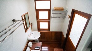Un baño pequeño y funcional con lavamanos, espejo, toallero y una mesita con artículos de aseo.