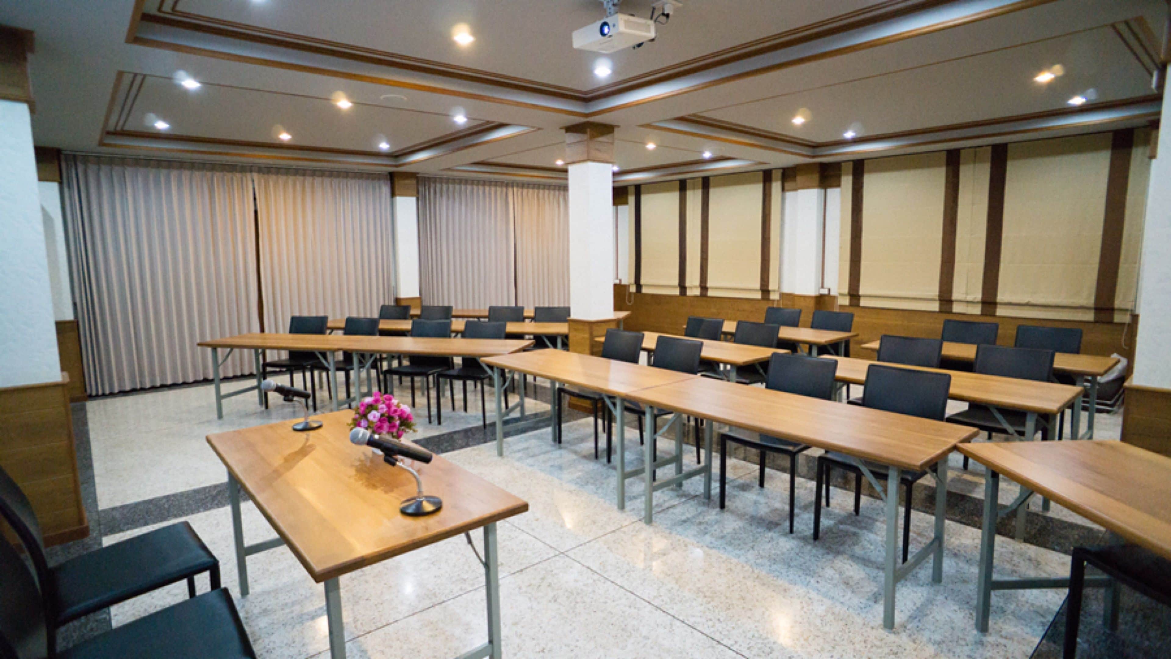 Un salón de conferencias con varias mesas y sillas, un atril y una pantalla de proyector.