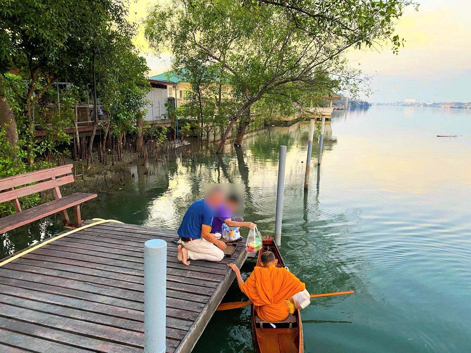 Een houten steiger die uitstulpt in een rustig wateroppervlak, met een persoon in een boot en een andere op de steiger.