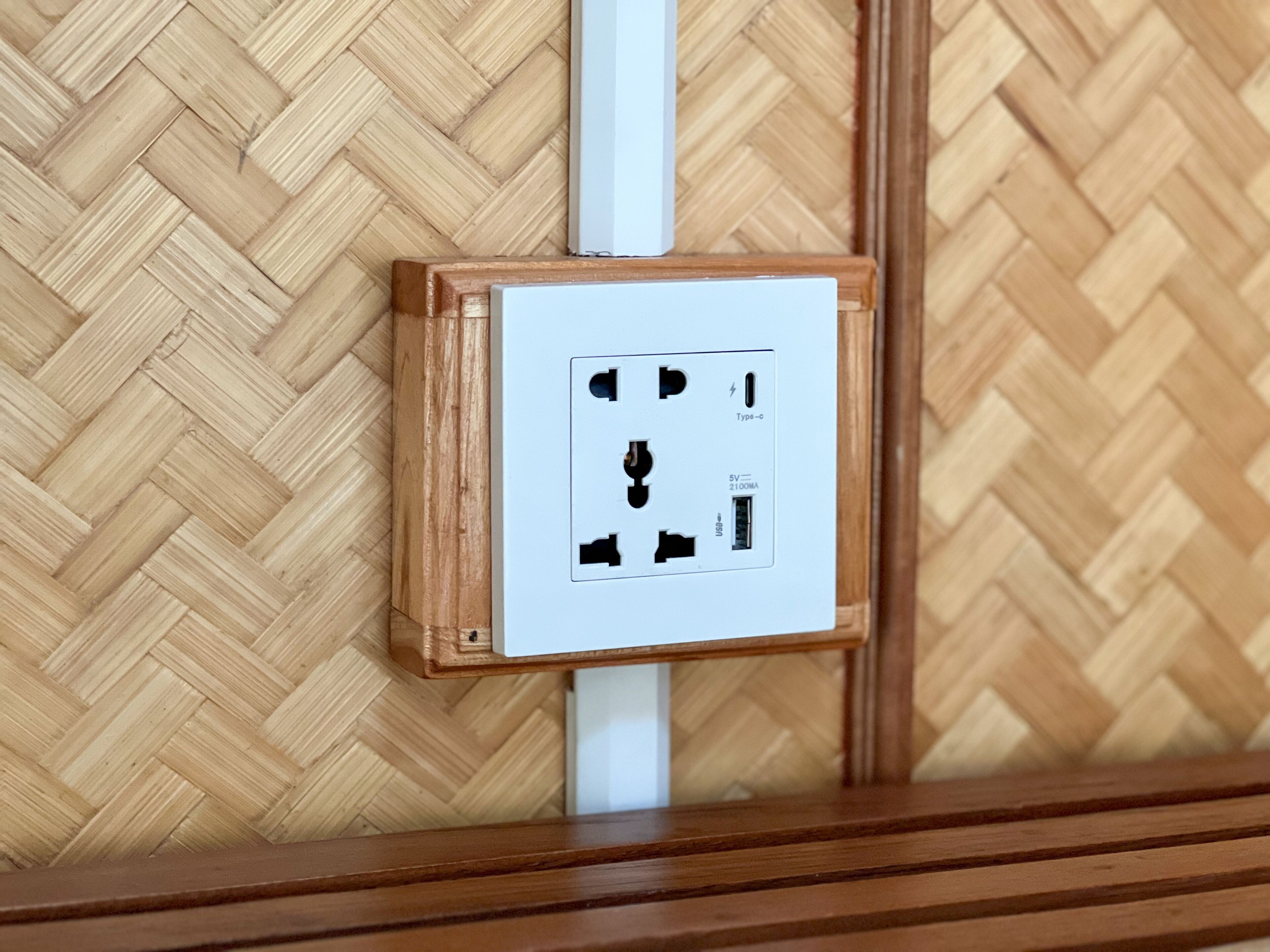 Un enchufe eléctrico instalado en la pared, con un marco de madera, frente a un revestimiento de madera con patrón de espiga.