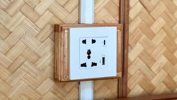 Un enchufe eléctrico instalado en la pared, con un marco de madera, frente a un revestimiento de madera con patrón de espiga.