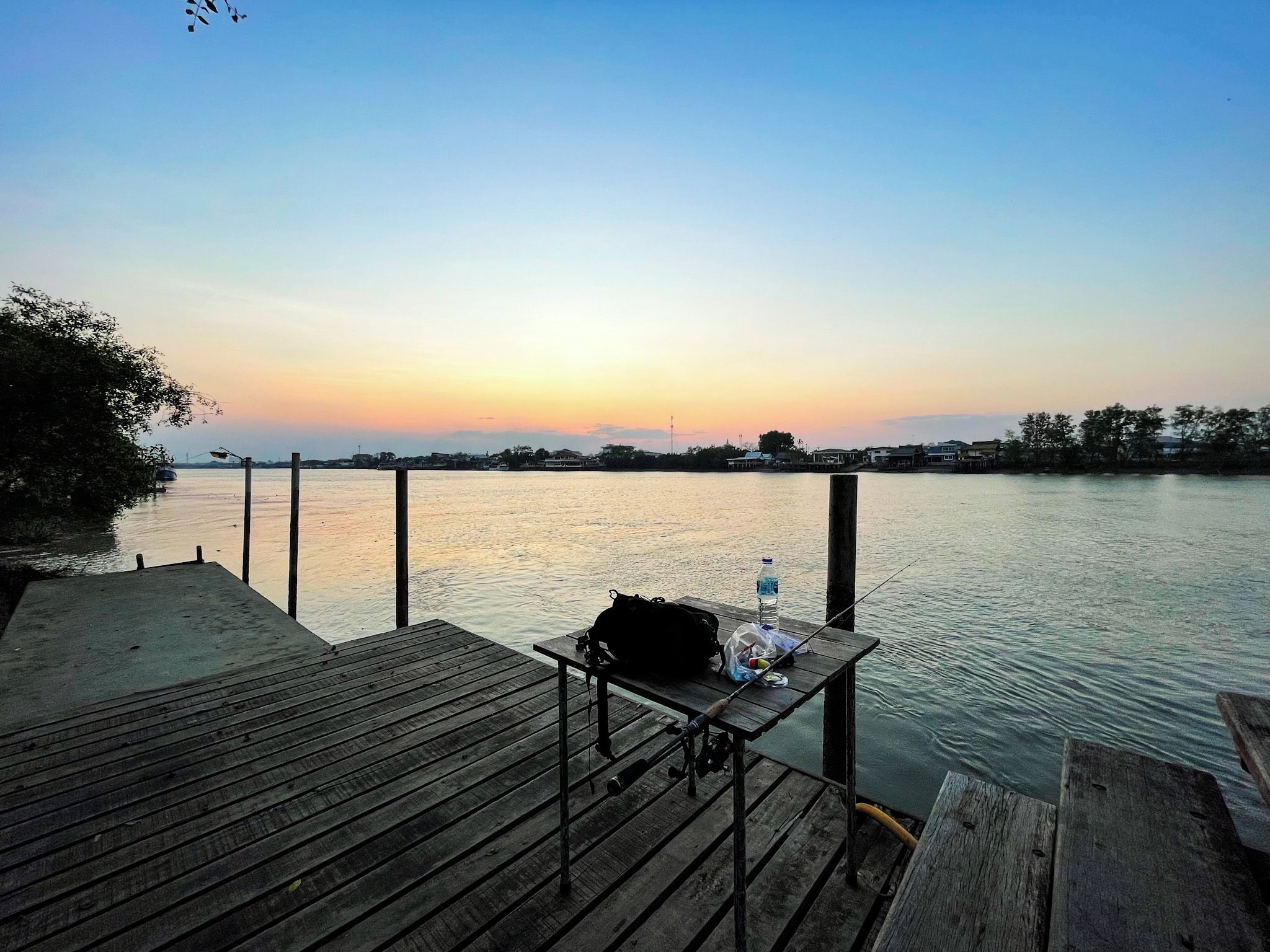 A wooden dock extending into calm water with a sunset in the background.