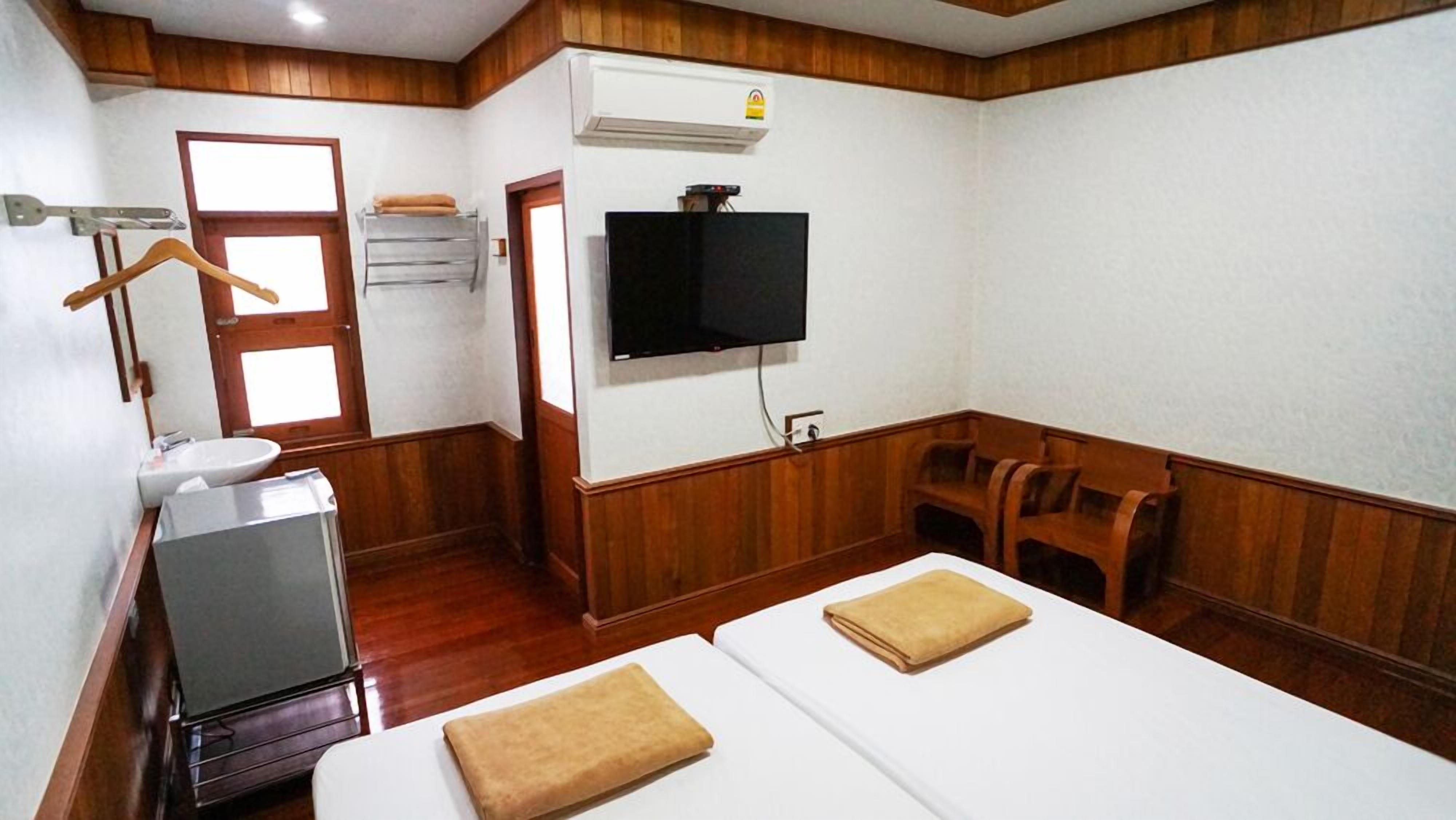 A hotel room with a wooden floor, a television mounted on the wall, a sink, and two beds with towels.