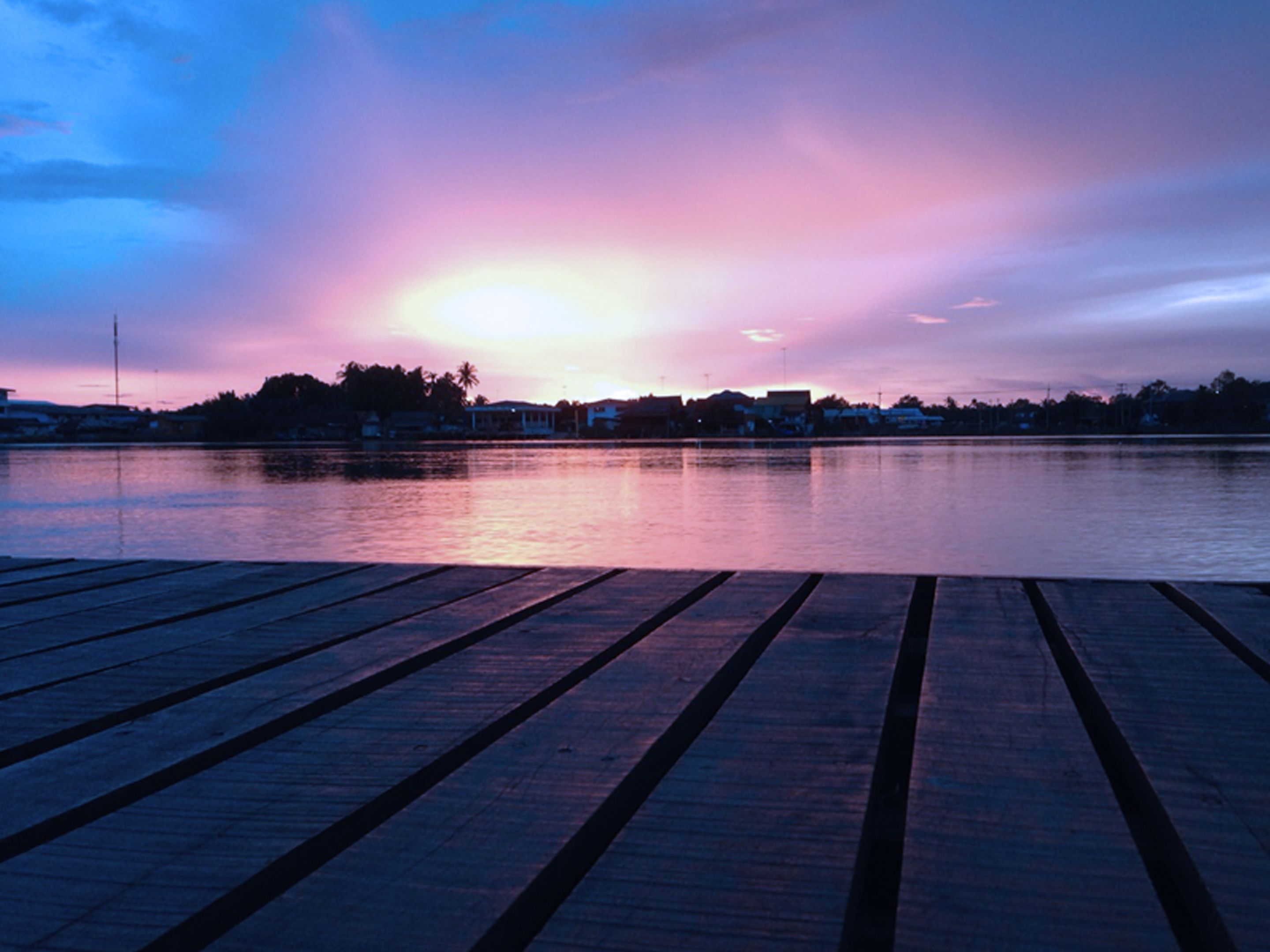 A wooden dock extending over calm water with a sunset in the background.