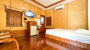 Habitación de hotel con piso de madera, una cama, un escritorio con una computadora, un lavamanos y un televisor montado en la pared.