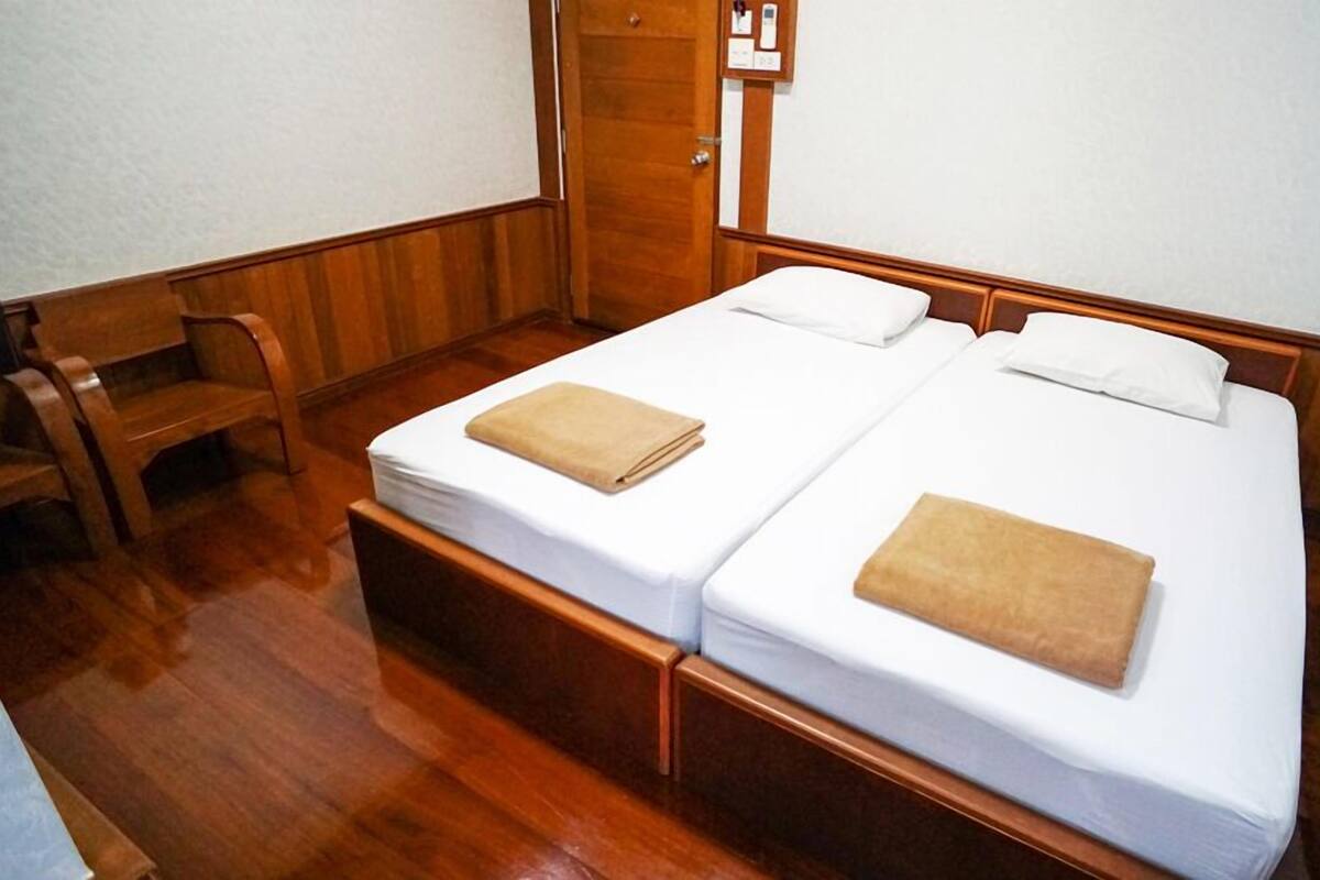 Ein Zimmer mit zwei Einzelbetten, Holzboden, einem Holzstuhl und einer Tür mit Schloss.