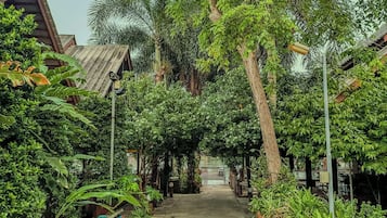 A pathway flanked by lush greenery and trees, leading to a building with a sloped roof.