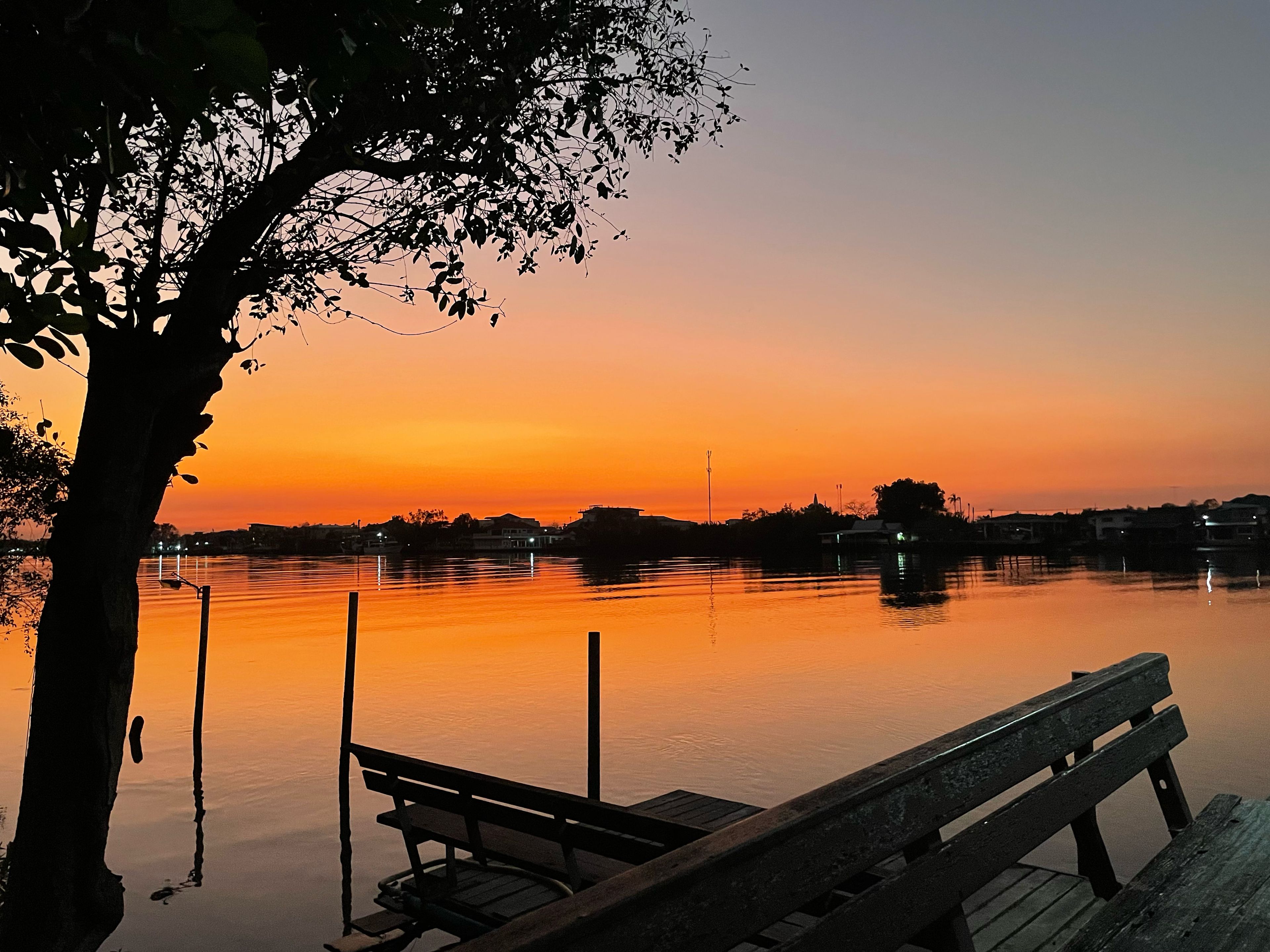 A calm body of water with a dock and benches, surrounded by trees and a sunset sky.
