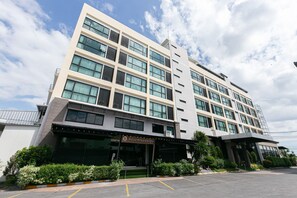 A multi-story hotel with a modern facade, large windows, and a well-maintained entrance area with a parking lot. - Grand Ratchapruek Hotel (Pak Kret)