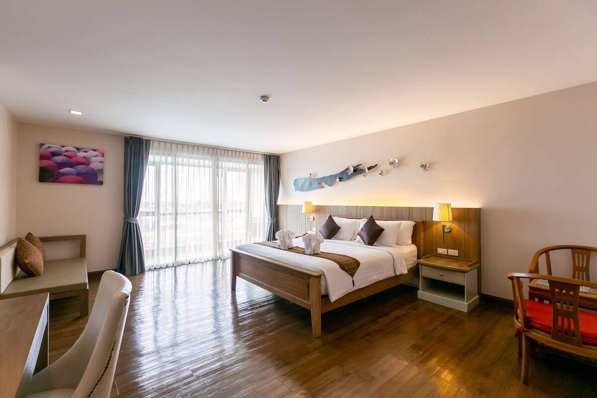 A hotel room with a large bed, bedside tables, a chair, a desk, and a window with curtains.