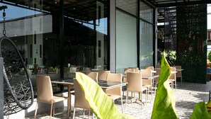 An outdoor cafe area with tables and chairs, a hanging chair, and potted plants. - Grand Ratchapruek Hotel (Pak Kret)